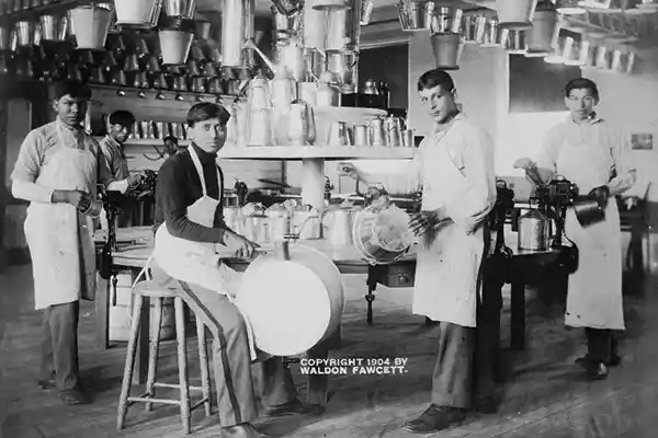 Young Native American men in metalworking workshop with pails, washtubs, watering cans, and other metal items. c1904